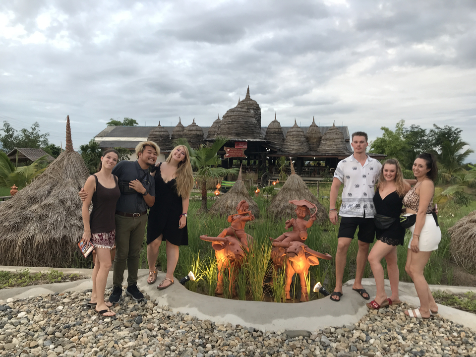 Group of friends posing in front of traditional architecture and greenery.