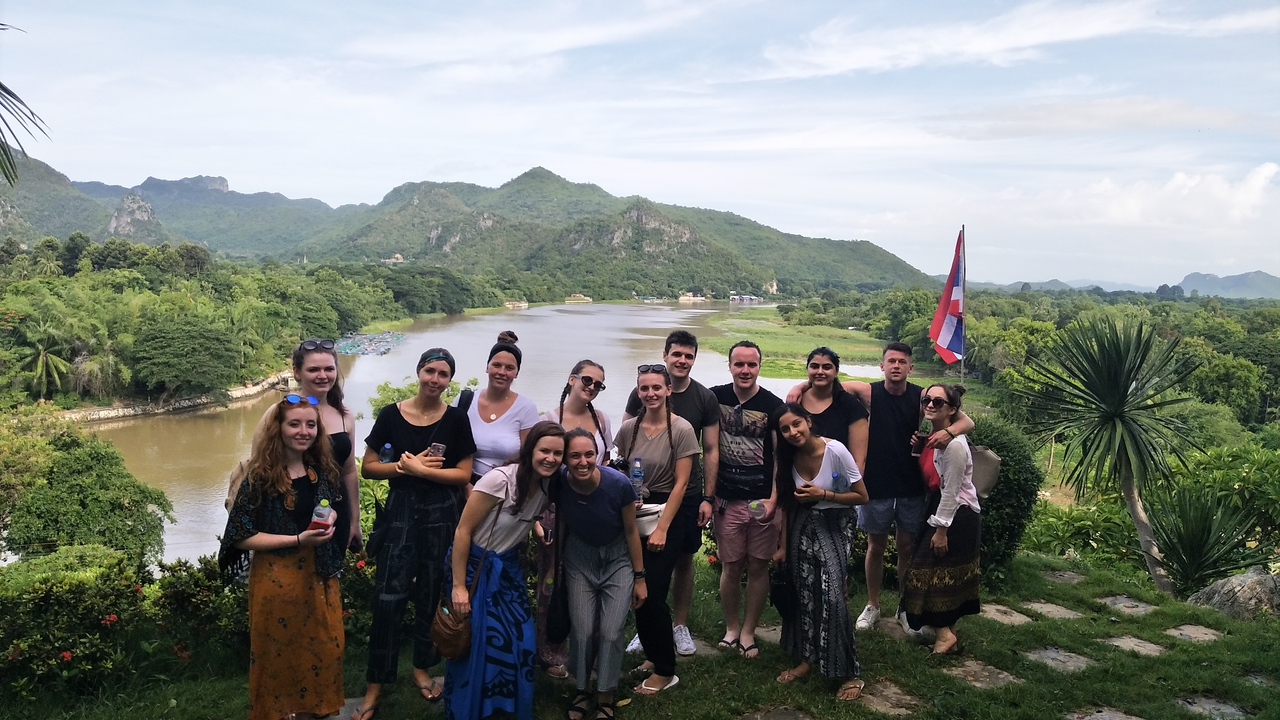 Group of people posing with a scenic view of river and mountains.