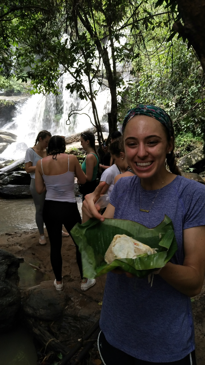 A woman eating in front of a waterfall with friends.