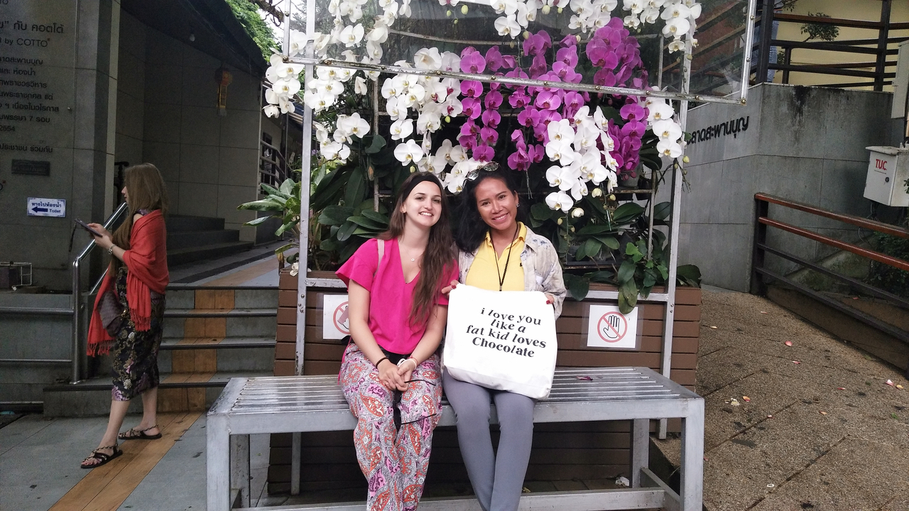 Two women sitting on a bench with flowers above them.