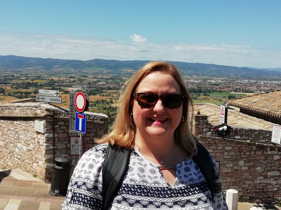 Femme souriante posant avec une vue panoramique en arrière-plan.