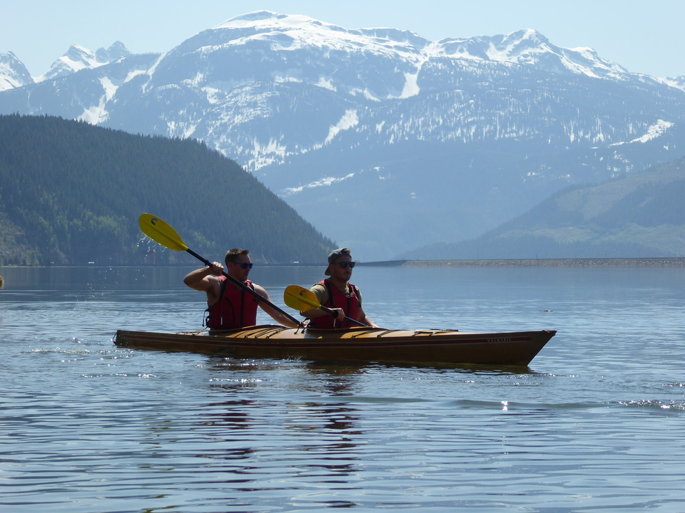 Zwei Personen fahren Kajak auf einem See mit Bergen im Hintergrund.