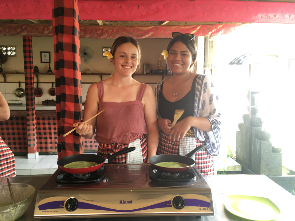 Two women cooking green pancakes on a stove.