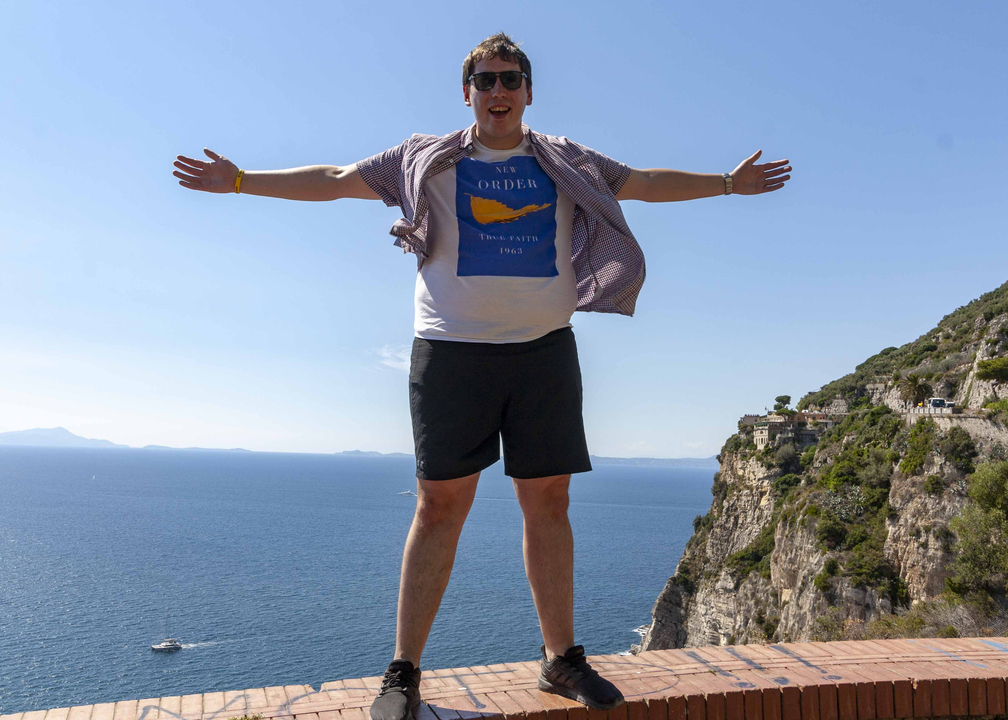 Personne posant au bord d'une falaise avec une vue panoramique sur la mer.
