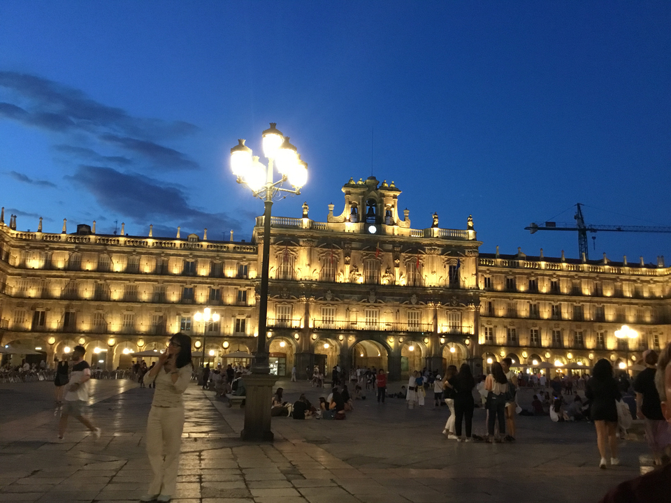 Bâtiment historique illuminé la nuit avec des personnes sur une place.
