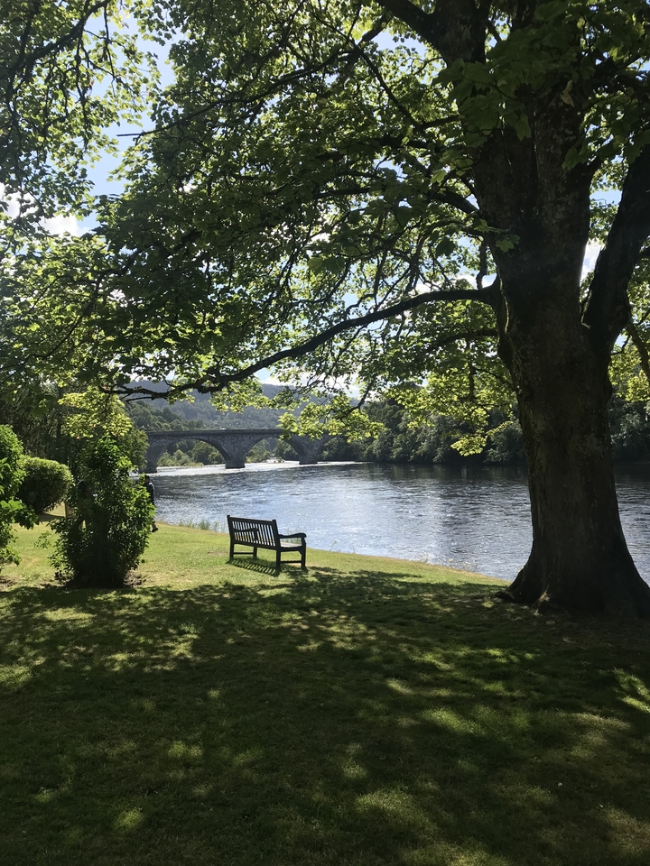 Vue panoramique sur la rivière avec un pont en pierre et un banc.