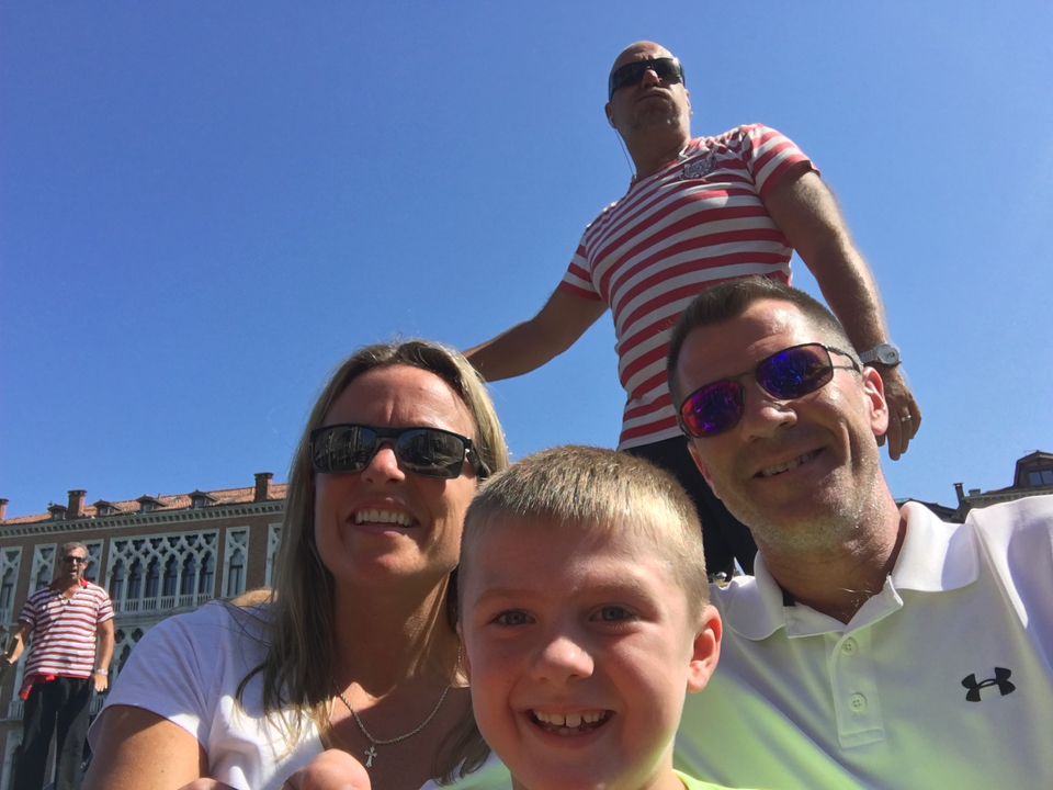 Famille souriante avec, à l'arrière-plan, des hommes en chemise rayée.