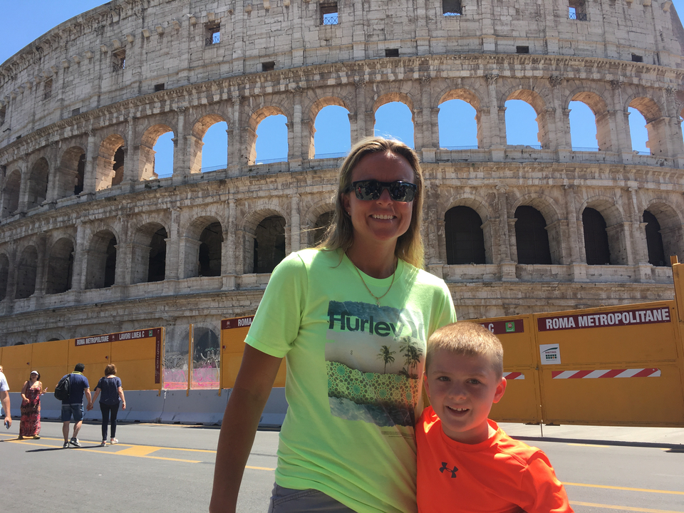Personne et enfant devant un grand colisée antique.