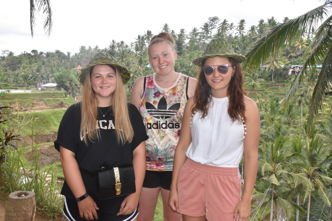 Three people posing with scenic terraced fields in the background.