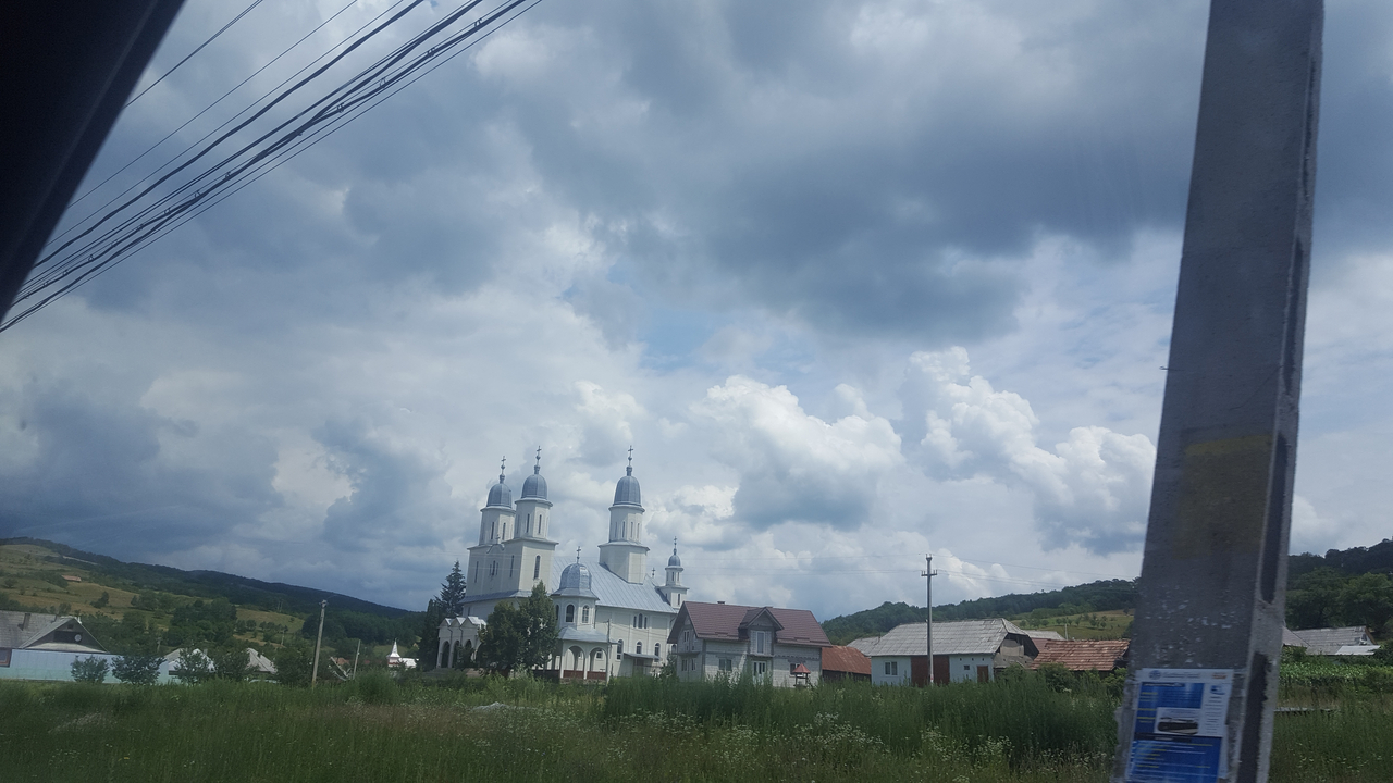 Vue d'une zone rurale avec une église blanche et un ciel nuageux.