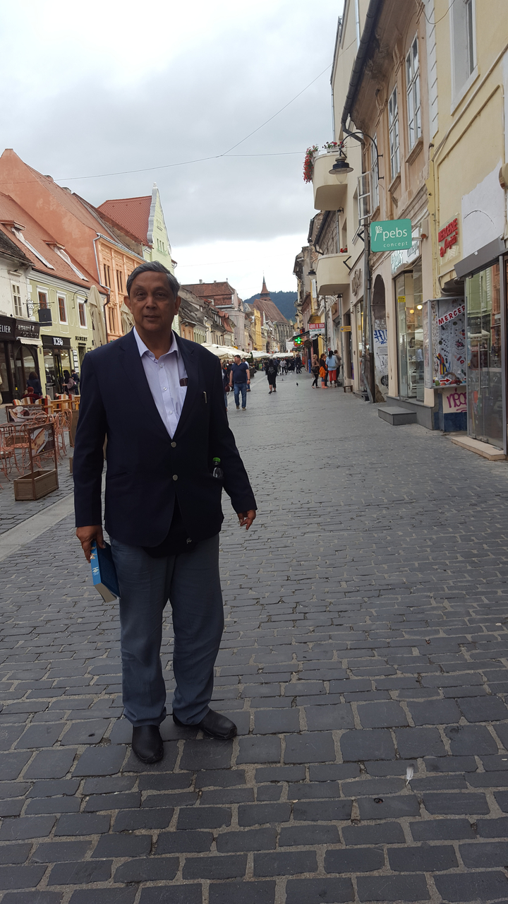 Homme debout dans une rue pavée entourée de boutiques.