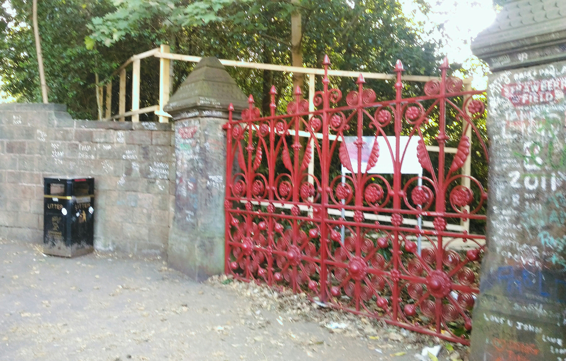 Portail ornemental rouge avec graffitis dans un parc.