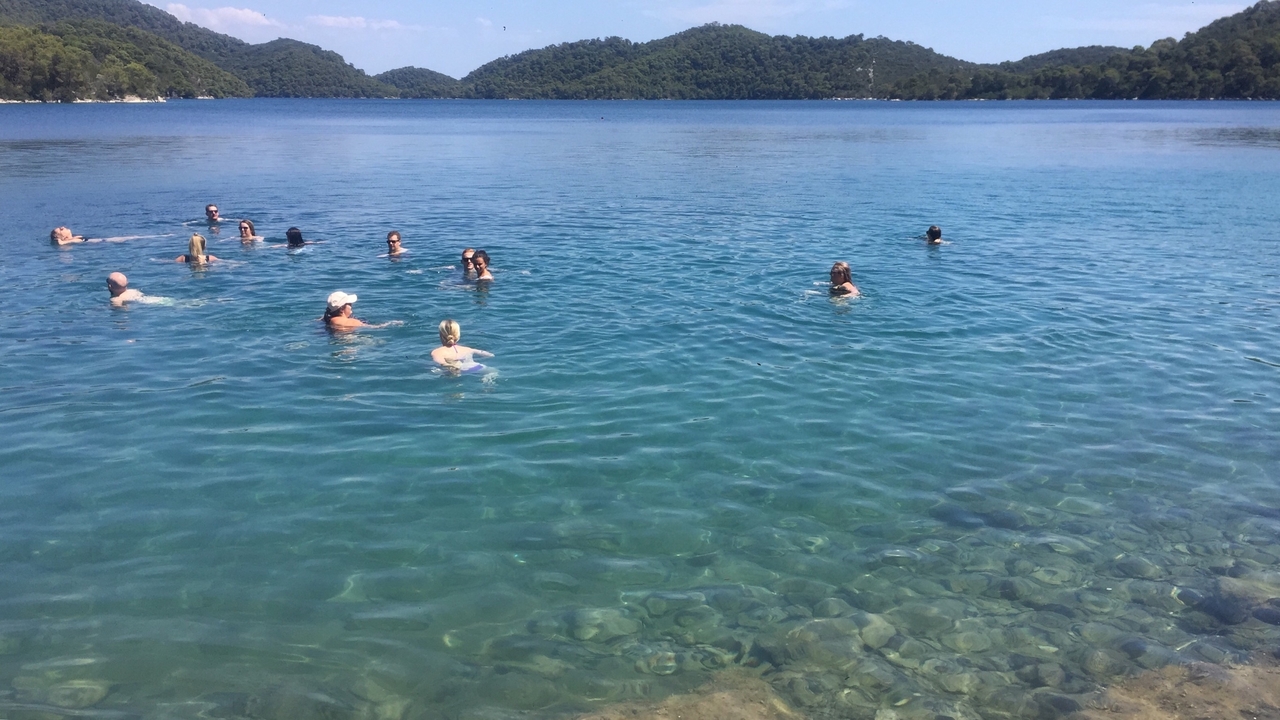 People swimming in a clear blue lake surrounded by hills.