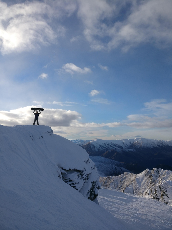 Personne tenant un snowboard sur un sommet enneigé.