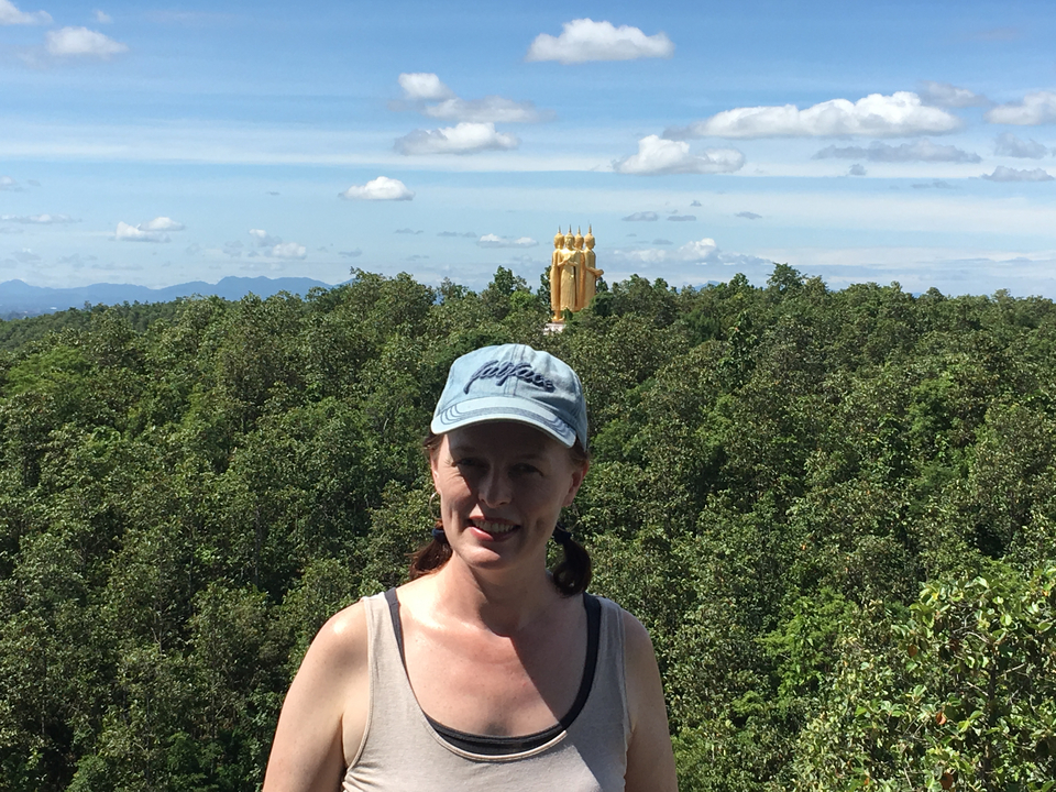 Femme posant avec une vue de paysage et une statue dorée en arrière-plan.