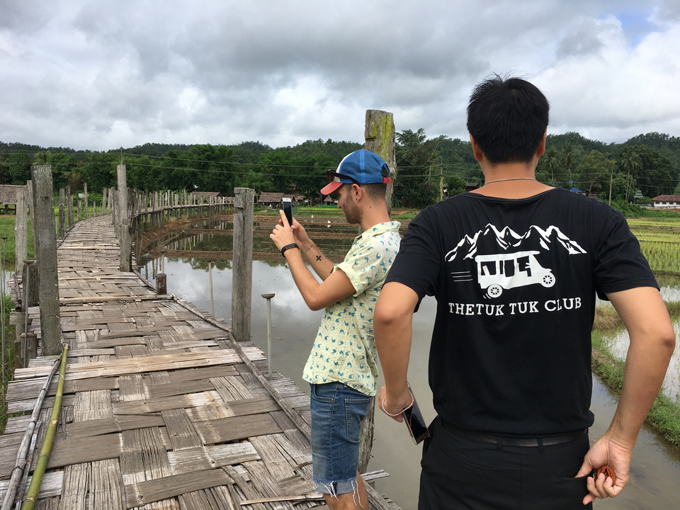 Deux personnes sur un pont de bambou au-dessus d'une rizière, en train de prendre des photos.