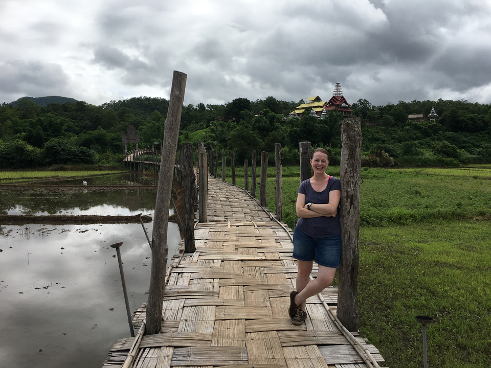 Femme souriante sur un pont de bambou au-dessus d'une rizière.