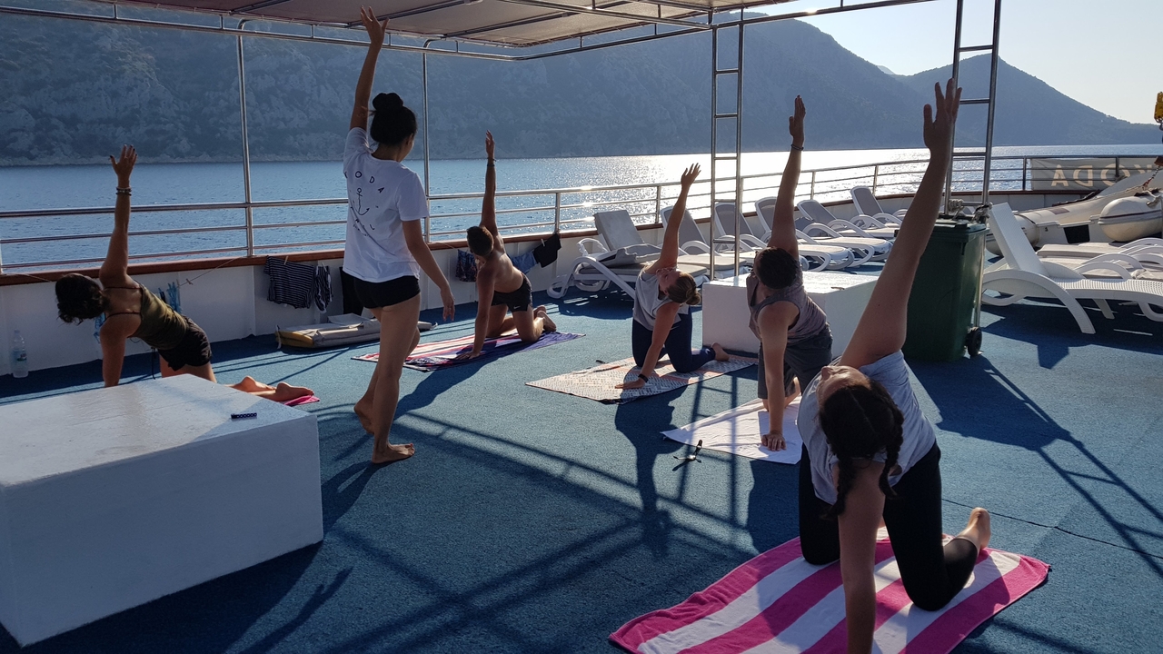 Group of people doing yoga on a boat deck against a beautiful seascape.