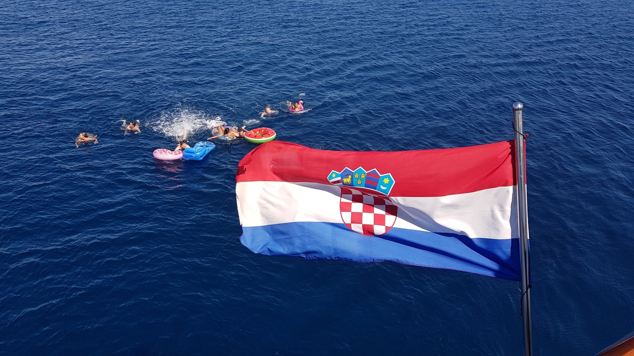 Drapeau croate flottant sur un bateau avec des personnes nageant dans la mer.