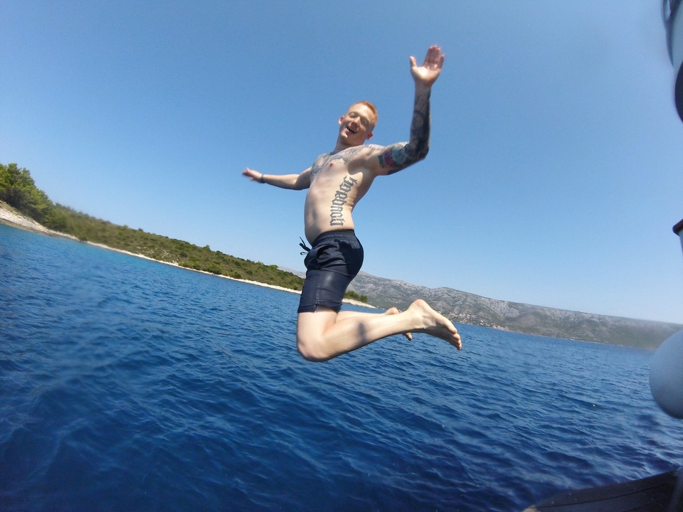 A man jumping into the air over clear blue water with a coastline in the background.