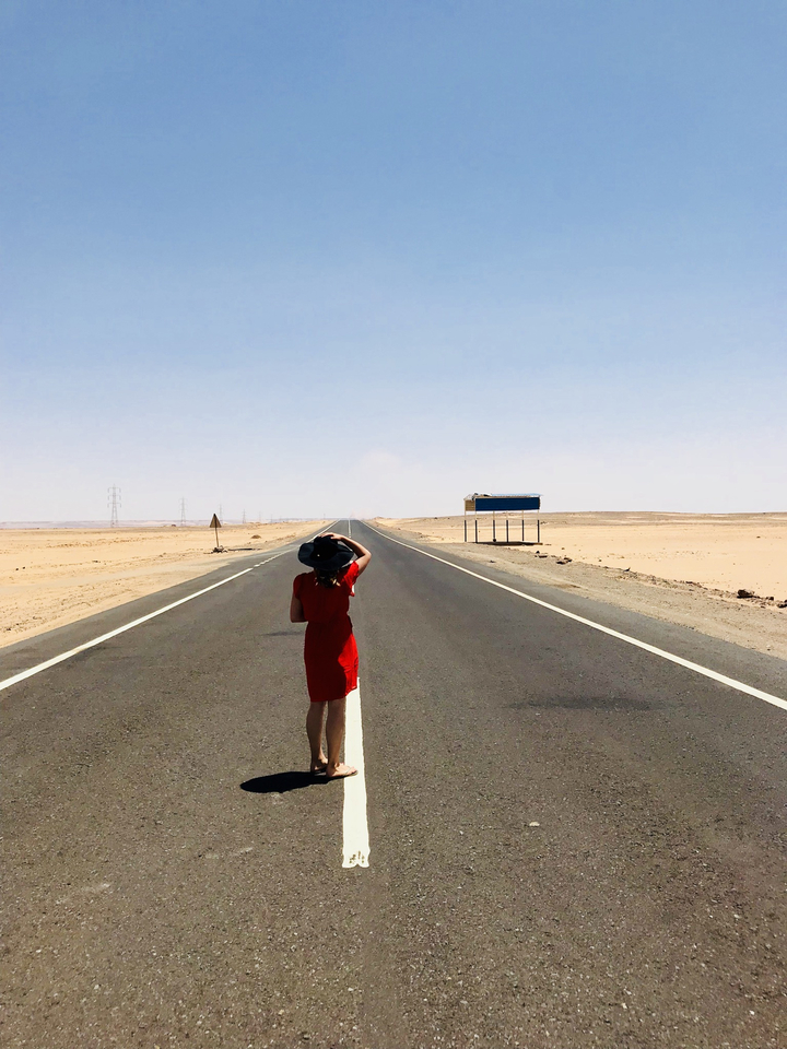 Personne en robe rouge debout sur une longue route désertique.