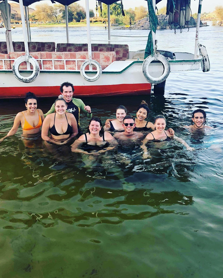 Group of people swimming in water near a boat.