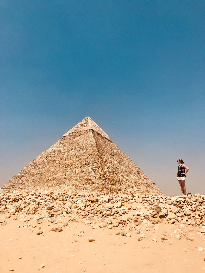 Person standing near a pyramid with clear blue sky.