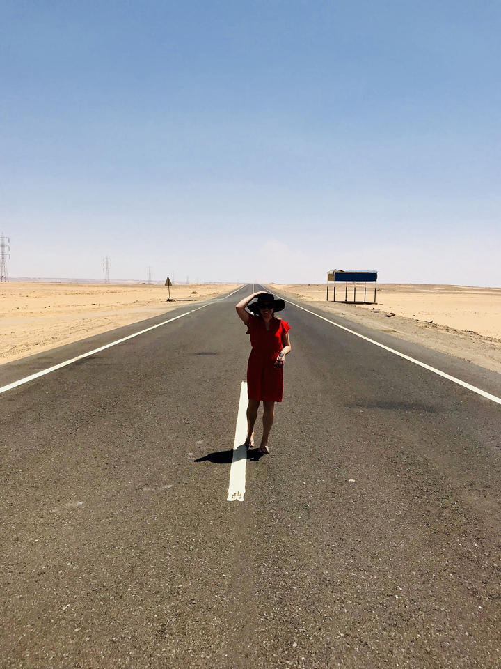 Personne en robe rouge debout sur une route du désert.