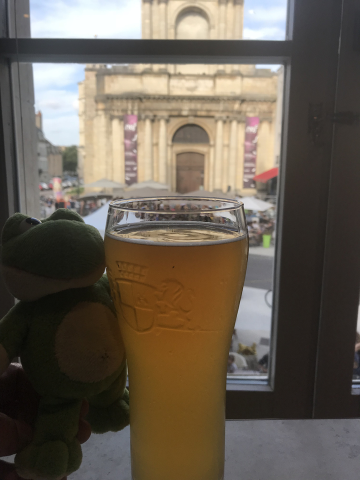 Vue d'un verre de bière et d'un petit jouet en peluche avec en arrière-plan une scène de rue.