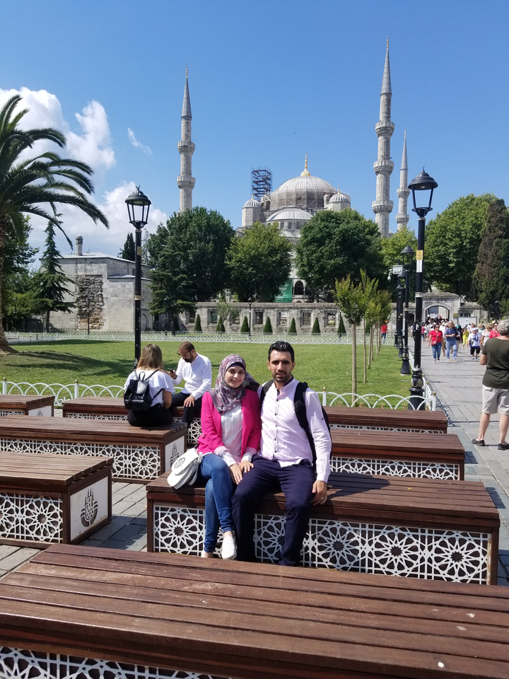 Deux personnes assises sur des bancs avec une mosquée en arrière-plan.