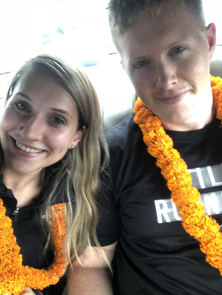 Deux personnes souriantes portant des guirlandes de fleurs traditionnelles.