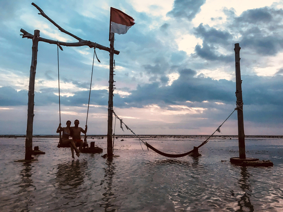 Two people sitting on swings in the ocean during sunset.