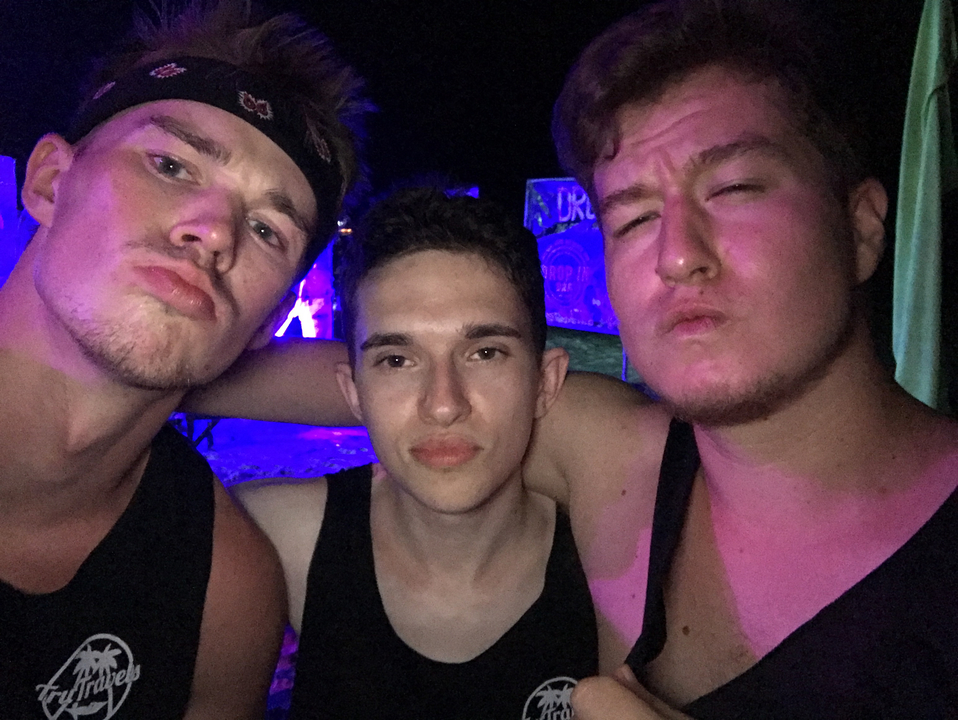 Three men posing at night under neon lights.
