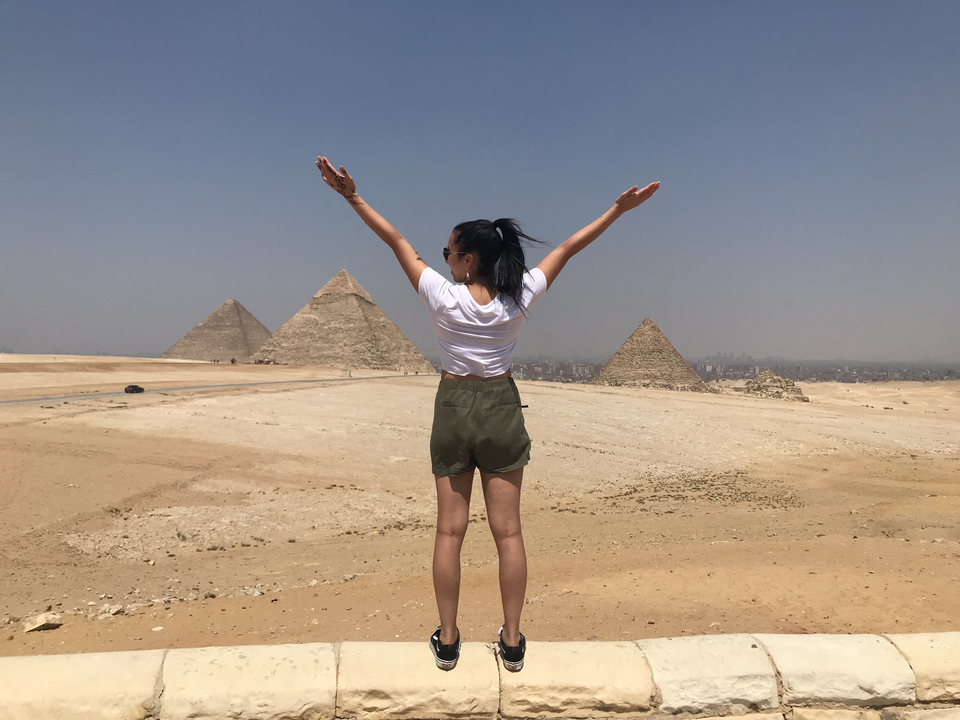 Personne levant les bras vers les pyramides dans le désert.