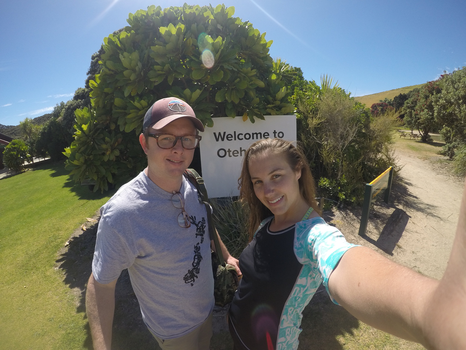Deux personnes prenant un selfie devant un panneau « Bienvenue à Otehi Bay ».