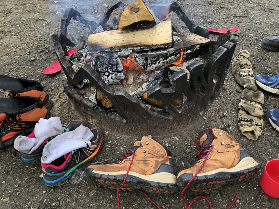 Feu de camp avec des chaussures de randonnée et des chaussettes autour.
