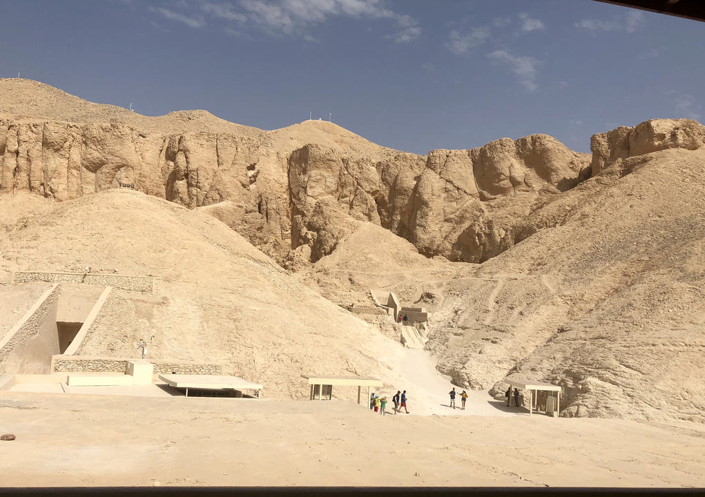 Des touristes explorent une vallée avec des ouvertures de tombeaux dans un paysage désertique.