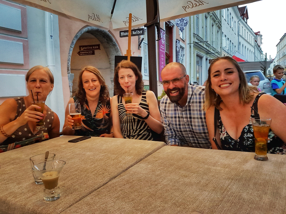 Groupe de personnes assises à un café en terrasse, souriantes et tenant des boissons.