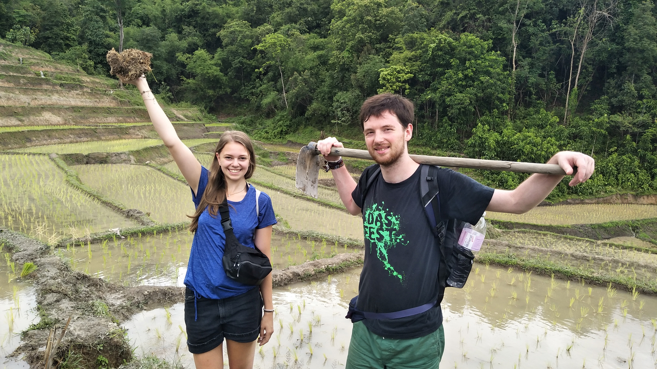 Two people holding tools in rice terraces.