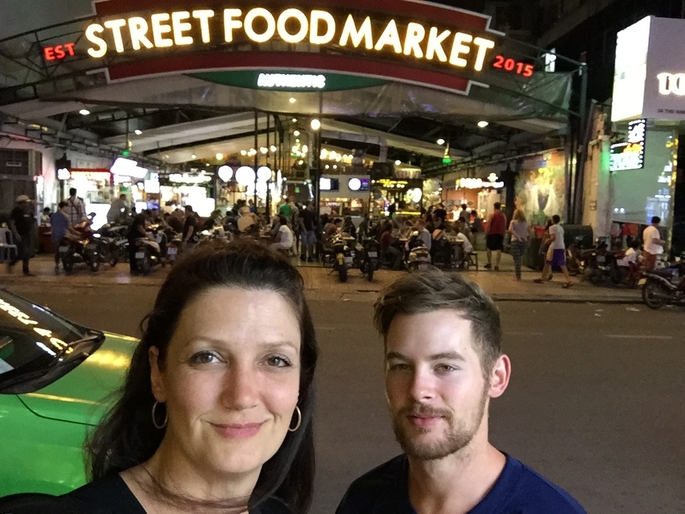 Selfie avec un marché de nuit animé en arrière-plan.