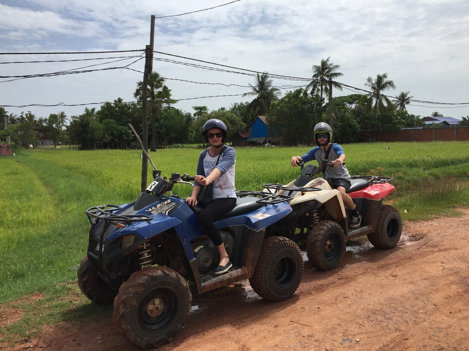 Deux personnes sur des quads roulant le long d'un sentier de terre dans une zone rurale.