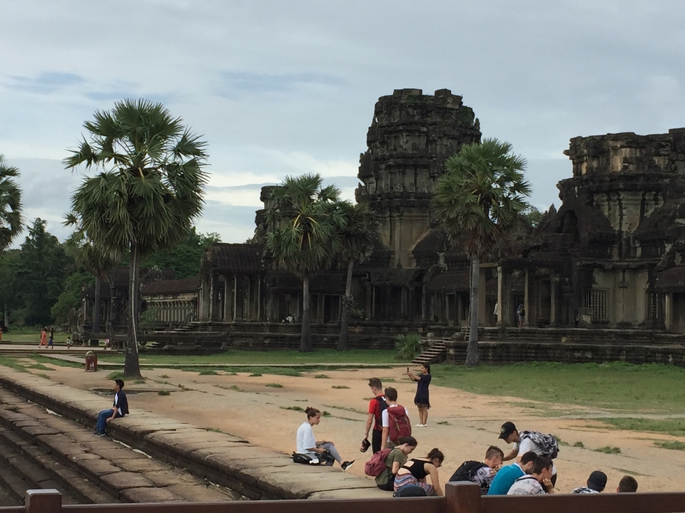Ruines d'un temple antique avec des palmiers et des visiteurs.