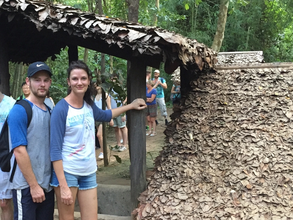 Des touristes visitant un site traditionnel avec un toit de feuillage.