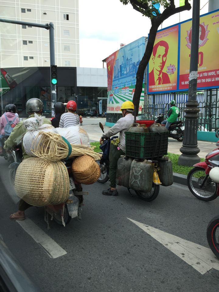 Des gens sur des motos, l'un transportant une variété de marchandises.