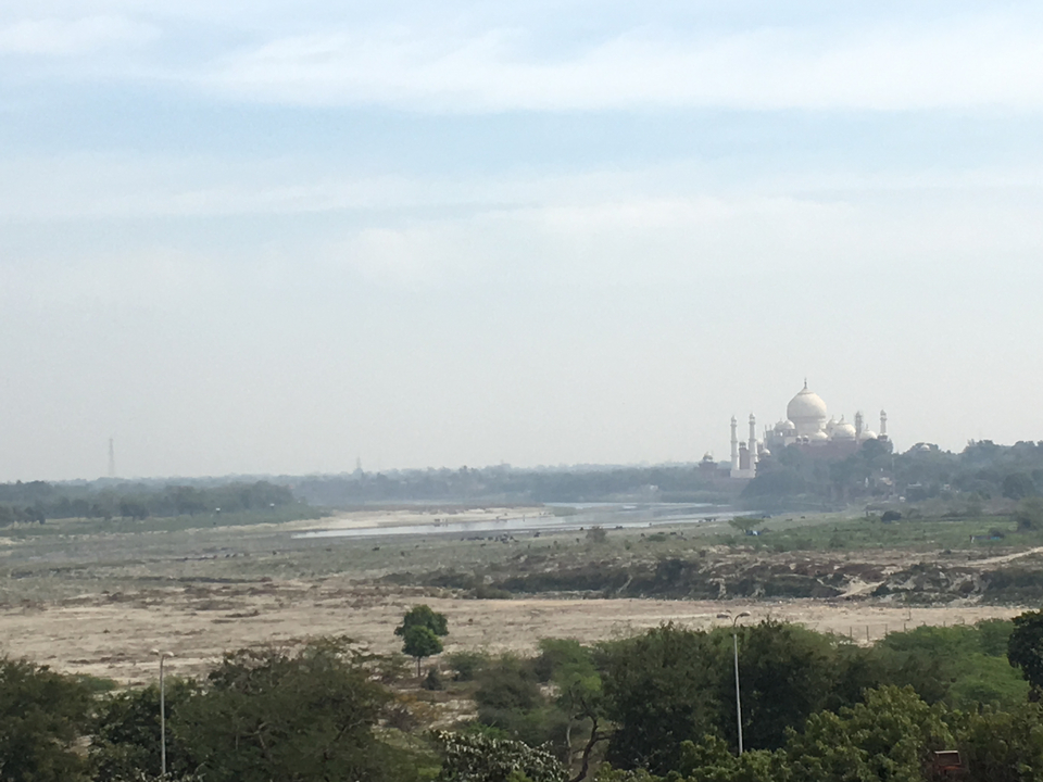 Vue lointaine du Taj Mahal au bord d'une rivière.