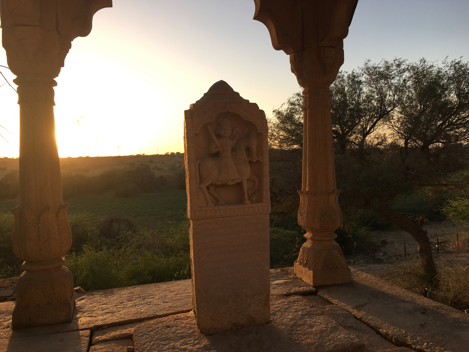 A statue with sunset in the background framed by pillars.