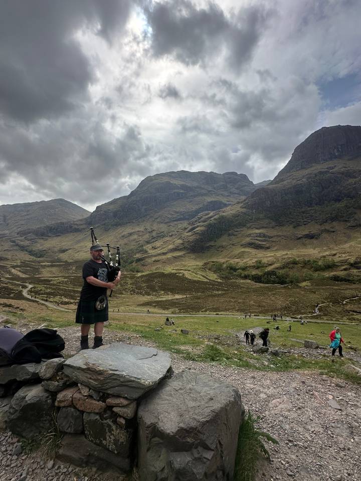 A man playing bagpipes in a scenic landscape.