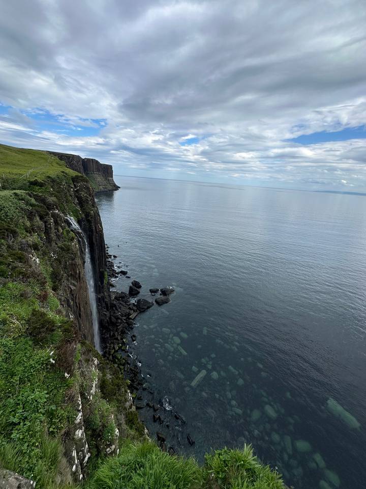 Cliffside view overlooking the ocean with a waterfall and rocky shore.