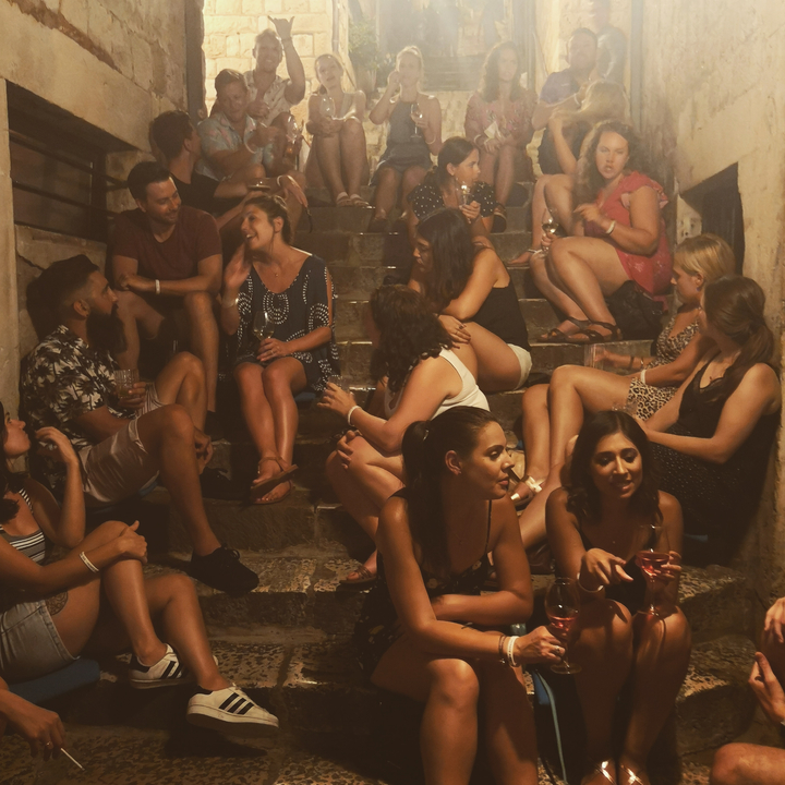 Groupe de personnes assises sur des marches savourant des boissons et une conversation.