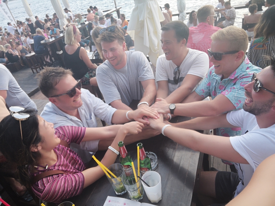 Groupe d'amis riant et interagissant à une table avec des boissons.